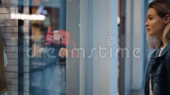 迷人的金发女郎站在商场的橱窗前视频的预览图