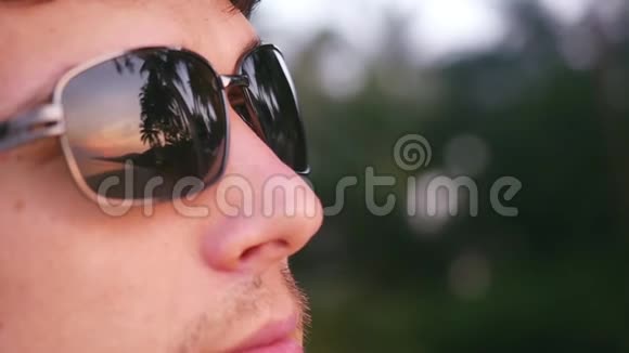 英俊的年轻时尚男士戴着太阳镜在热带海滩上看起来日落慢动作1920x1080视频的预览图