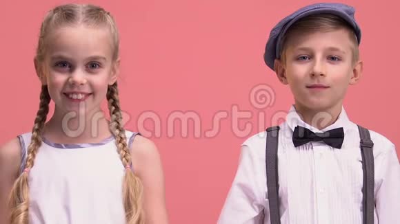 活泼开朗的小男孩和小女孩看着镜头被孤立在粉红色的背景上视频的预览图
