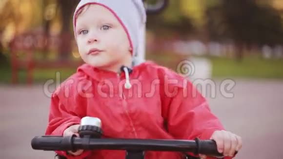 可爱的小男孩坐在自行车上保持手在车轮上穿红色夹克准备骑自行车的孩子视频的预览图