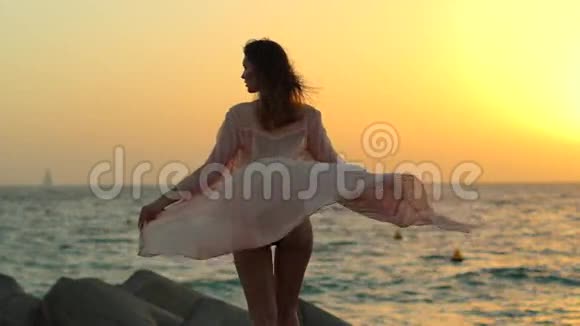 在迪拜的石头海滩上女孩在日落时玩一件连衣裙视频的预览图