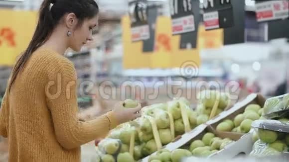 年轻的女人在超市里选择了一个绿色的苹果拿着一个水果然后放进包裹里4K视频的预览图