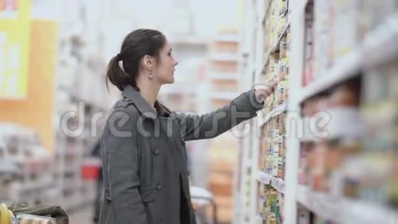 年轻漂亮的女人站在货架前拿着一个罐头试着在超市里选择4K视频的预览图
