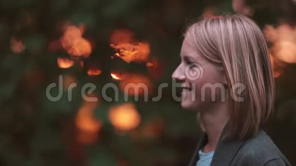 年轻美丽的女人站在公园的夕阳下微笑着享受着大自然特写镜头侧视视频的预览图