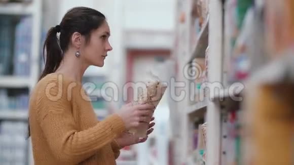 年轻漂亮的女人站在架子前抱着一个试着在超市里选择一些东西4K视频的预览图