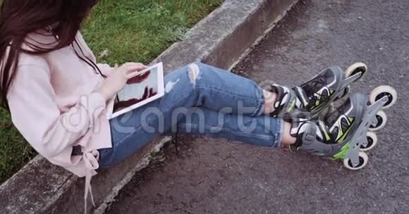 一个年轻女孩穿着粉红色背心蓝色牛仔裤坐在绿草上使用触摸屏视频的预览图