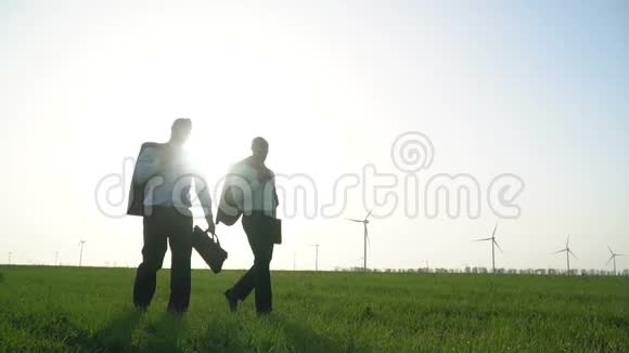 穿着商务服的男人在风力发电机附近的一片绿色草地上行走其中一个人正在扔出一个视频的预览图