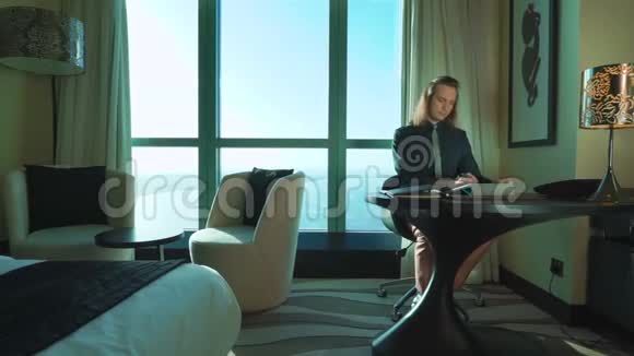 一位留着长发的年轻商人正在家里办公室或酒店做平板电脑打字思考打电话视频的预览图