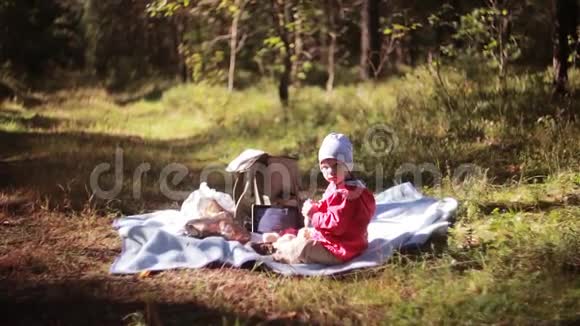 可爱的小男孩秋天在森林里野餐坐在草地上看着相机侧视视频的预览图