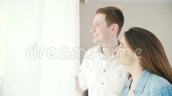 一对幸福而相爱的夫妇正站在窗边挂着窗帘视频的预览图