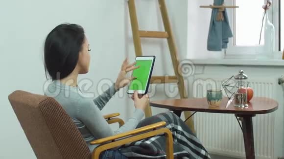 美丽的女孩使用平板电脑和绿色屏幕坐在舒适的椅子上的家视频的预览图