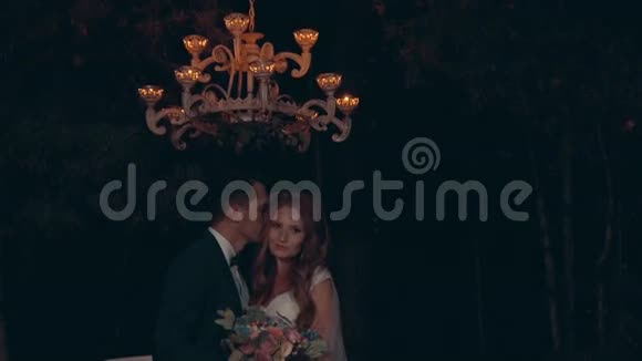 新婚夫妇夜以继日地拥抱站在枝形吊灯下灯光照在漆黑的森林里视频的预览图