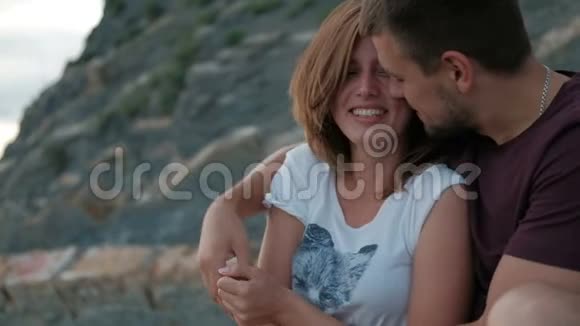 在夏天的户外一个年轻人拥抱坐在海岸上的女人视频的预览图