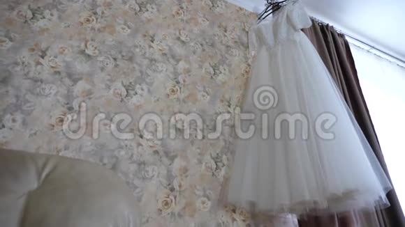 漂亮的白色婚纱挂在窗前的衣架上视频的预览图