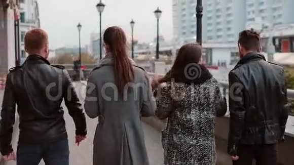 两个时髦的女孩和两个时髦的男人兴高采烈地在城市里散步和交谈慢影稳拍后景视频的预览图