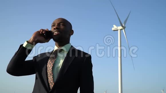 一个穿商务服的黑人通过电话沟通一个风力发电机背景视频的预览图