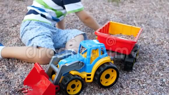 可爱的幼儿男孩在操场上玩玩具拖拉机和拖车视频的预览图