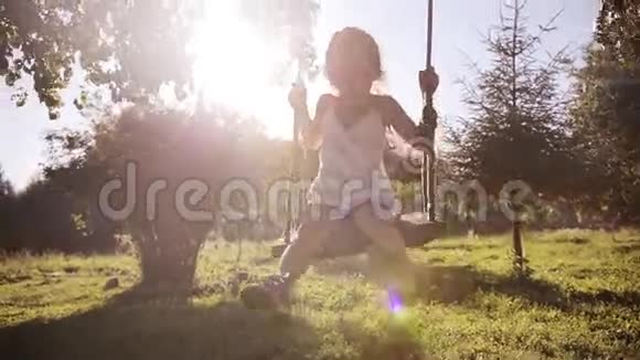 可爱的小女孩在树上荡秋千时玩得很开心日落时在公园里微笑视频的预览图