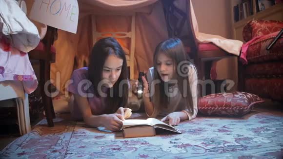 两个可爱的女孩晚上躺在地板上读一本书视频的预览图