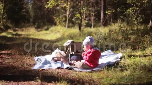 可爱的小男孩秋天在森林里野餐坐在草地上在户外吃饭侧视视频的预览图