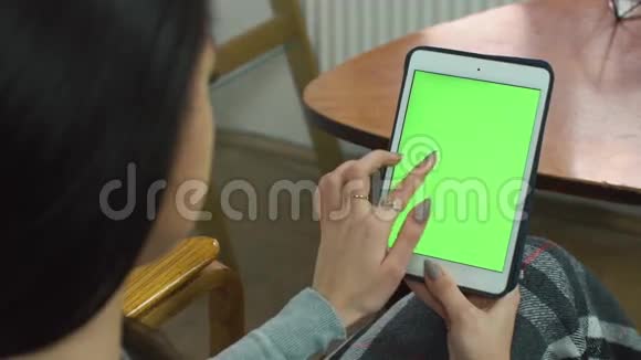 美丽的女孩使用平板电脑和绿色屏幕坐在舒适的椅子上的家视频的预览图