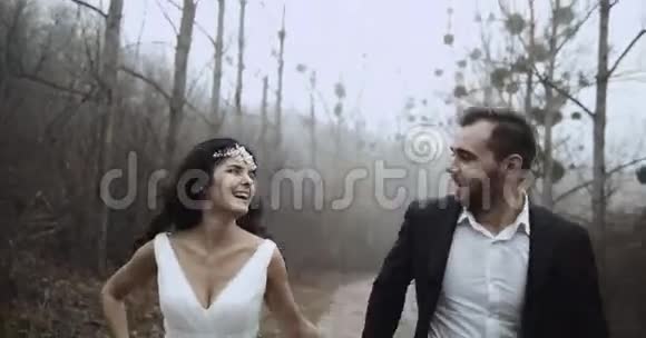 新婚快乐的新婚夫妇牵着手跑着在森林里互相看着视频的预览图