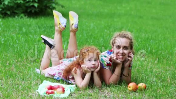 可爱的红头发的小女孩和她的母亲躺在草坪上视频的预览图