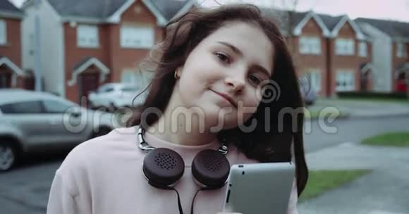 戴着耳机和平板电脑的漂亮年轻女孩在看相机女孩拿着平板电脑在前面视频的预览图