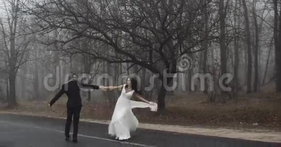 新郎新娘在靠近森林的路上带着情感跳舞玩耍慢悠悠4k视频的预览图