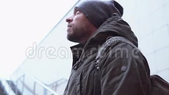 年轻迷人的男人穿着夹克和帽子独自站在街上在寒冷的一天环顾四周4K视频的预览图