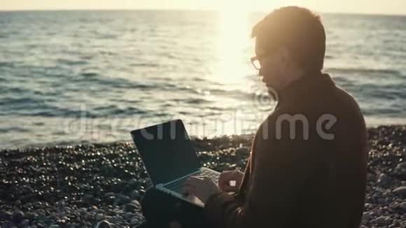 成年男子在手提电脑上工作商人坐在海边视频的预览图