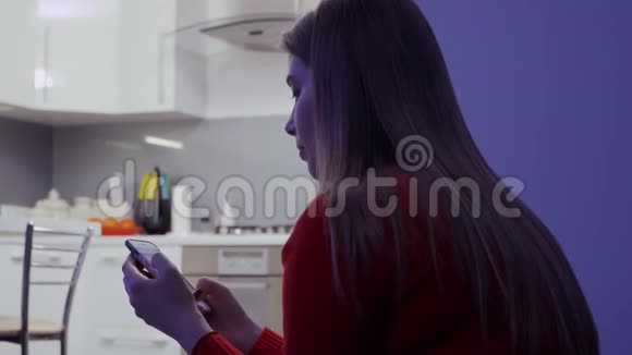 穿着毛衣的年轻女孩正在厨房和朋友聊天视频的预览图