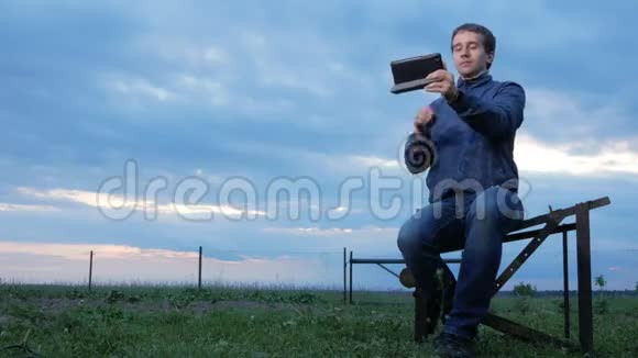 日落时分一个年轻人坐在石碑上聊天后面一片绿草地美丽的天空视频的预览图