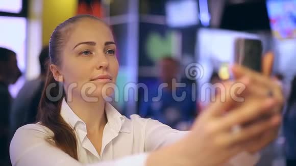 一个年轻的女人坐在快餐店里拍自拍在智能手机屏幕上看她的照片视频的预览图