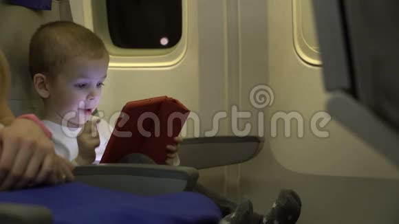 两岁的男孩在平板电脑上玩坐在飞机座位上视频的预览图