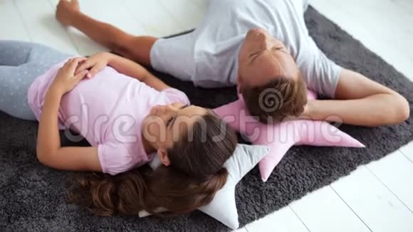 积极的父亲和他的小女儿躺在地板上视频的预览图