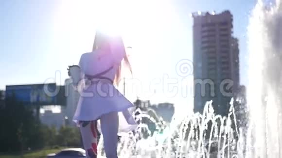 那个女孩站在喷泉的边缘在明亮的阳光下喝着咖啡慢动作高清高清视频的预览图
