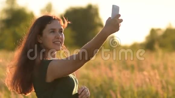年轻女子在手机上拍了一张自我肖像在田野里微笑视频的预览图