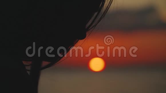 一个年轻女人坐在河边在日落时读一本书的剪影特写慢动作视频的预览图