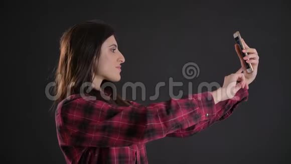 年轻美丽的白种人长发女孩在黑色背景下使用智能手机制作自拍照片的肖像视频的预览图