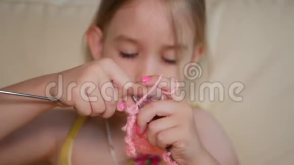 小女孩坐在沙发上编织羊毛围巾小女孩在家里用针编羊毛衣服视频的预览图