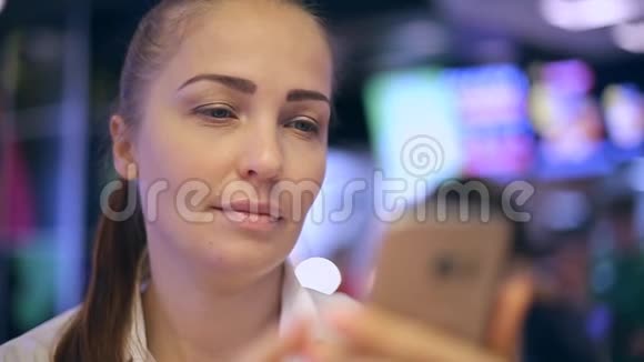 一个年轻的女人坐在快餐店里拍自拍在智能手机屏幕上看她的照片视频的预览图