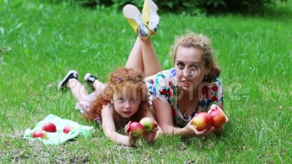 一个红头发的小女孩和她的在绿色的夏日公园的草坪上玩苹果视频的预览图