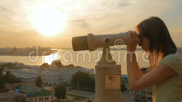 年轻女子透过观光望远镜在日落时分探索城市视频的预览图