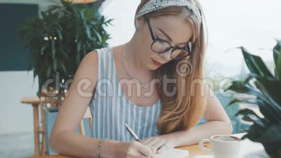 年轻的金发女人做白日梦在她的日记里写日记女人在咖啡馆的笔记本上写字视频的预览图