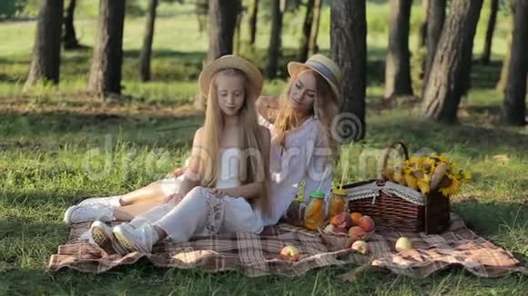 一位快乐的母亲和幸运的女儿一起坐在城市公园里玩在日落的温暖的夜晚野餐视频的预览图