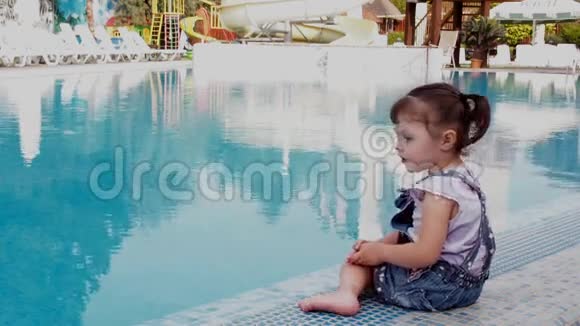 蓝色游泳池旁的小女孩一个小孩子在游泳池旁边玩一个漂亮的小女孩正坐在一个视频的预览图