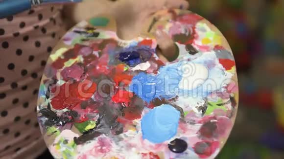 女艺术家用画笔在调色板上手工混合丙烯酸颜色视频的预览图