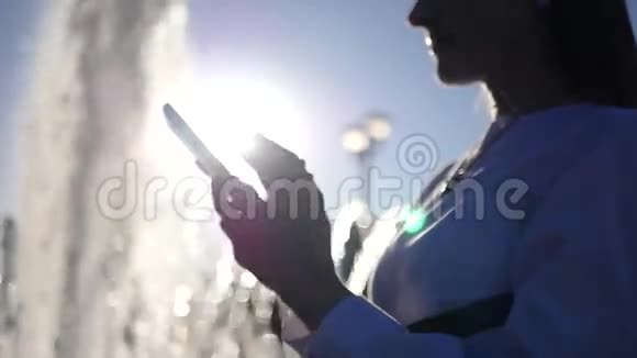 年轻漂亮的女孩站在喷泉前手里拿着一个电话写着一条信息从喷泉中消失视频的预览图