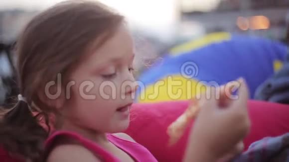 夏天美丽可爱的小女孩坐在豆袋椅子上在公园里吃披萨侧视视频的预览图